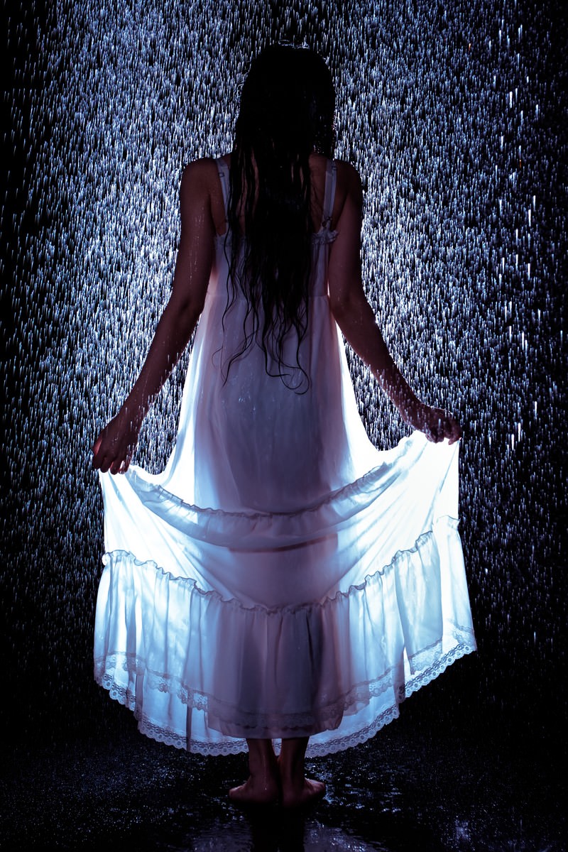 「雨に濡れてワンピースの裾をあげる女性の後ろ姿 | フリー素材のぱくたそ」の写真［モデル：緋真煉］