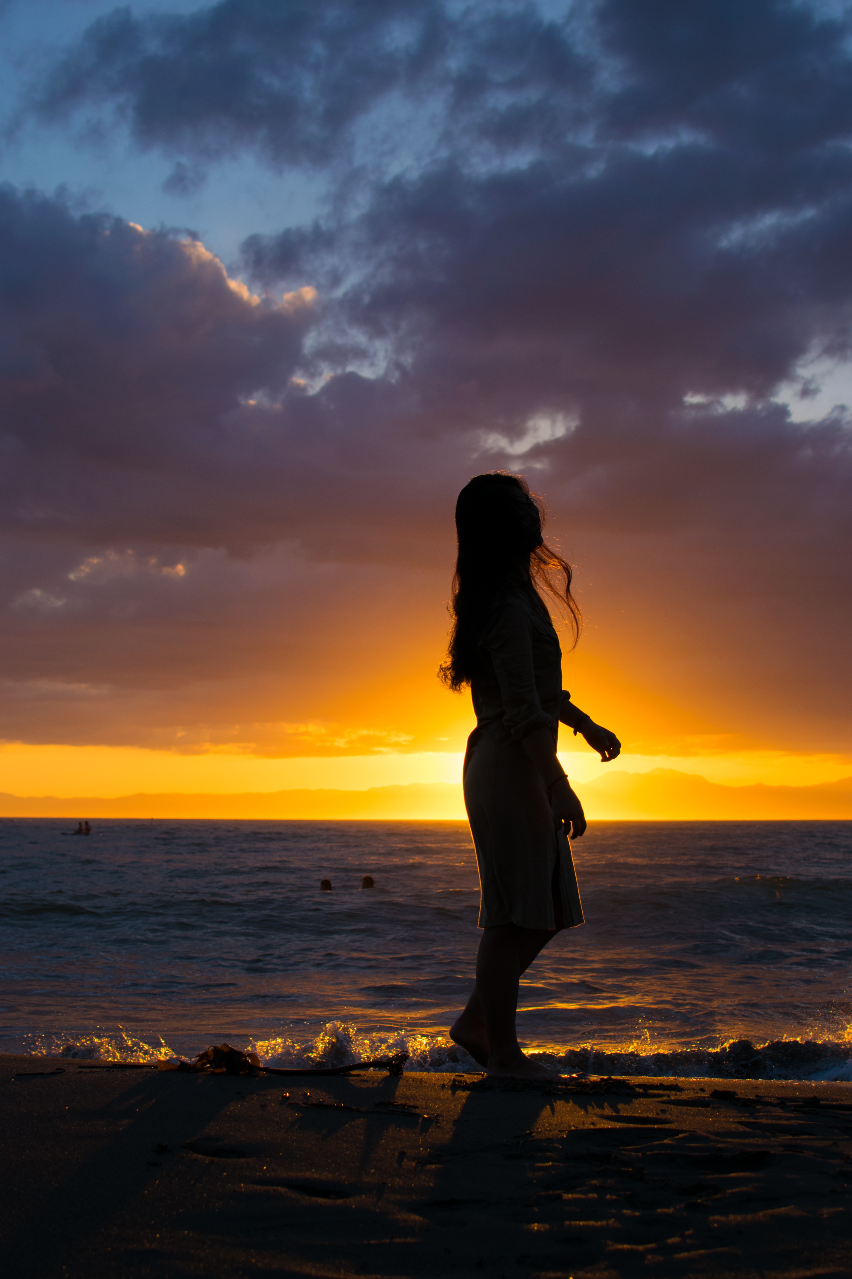 夕日に照らされる砂浜を歩く女性のシルエットの写真素材